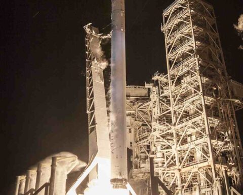 A SpaceX Falcon 9 rocket launches the EchoStar XXIII satellite into a clear blue sky, with intense exhaust plume visible.