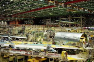 Boeing aircraft manufacturing facility showing multiple planes in various stages of assembly on the factory floor.