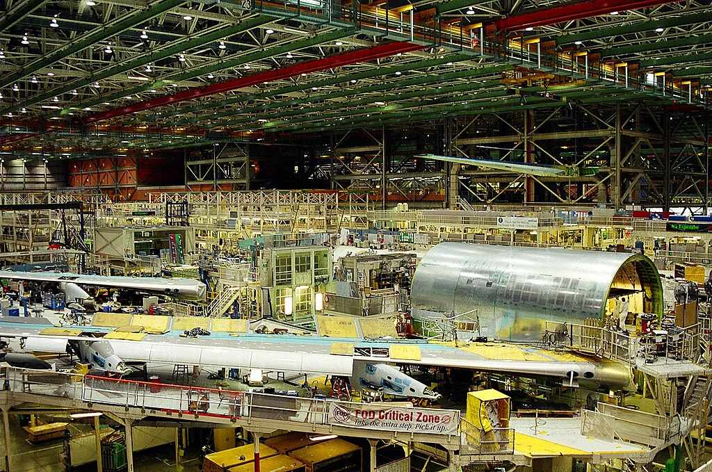 Boeing aircraft manufacturing facility showing multiple planes in various stages of assembly on the factory floor.