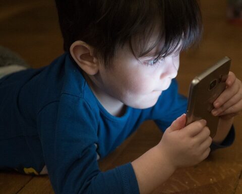 Young boy in blue shirt looking down at smartphone screen while sitting at wooden table