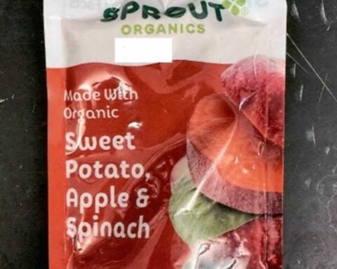 Sprout Organics Sweet Potato Apple and Spinach baby food pouch showing front packaging with green cap and colorful vegetable imagery on dark surface