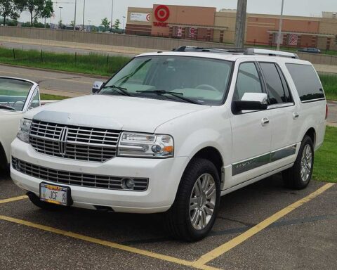 White Lincoln Navigator SUV parked in a parking lot with grass and buildings visible in the background