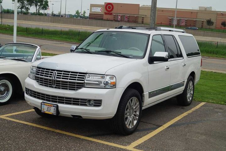 White Lincoln Navigator SUV parked in a parking lot with grass and buildings visible in the background