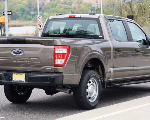 A gray 2021 Ford F-150 SuperCrew pickup truck parked on a street, showing the rear three-quarter view with visible tailgate, taillights, and bed.