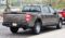 A gray 2021 Ford F-150 SuperCrew pickup truck parked on a street, showing the rear three-quarter view with visible tailgate, taillights, and bed.