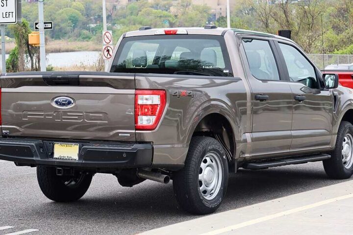 A gray 2021 Ford F-150 SuperCrew pickup truck parked on a street, showing the rear three-quarter view with visible tailgate, taillights, and bed.