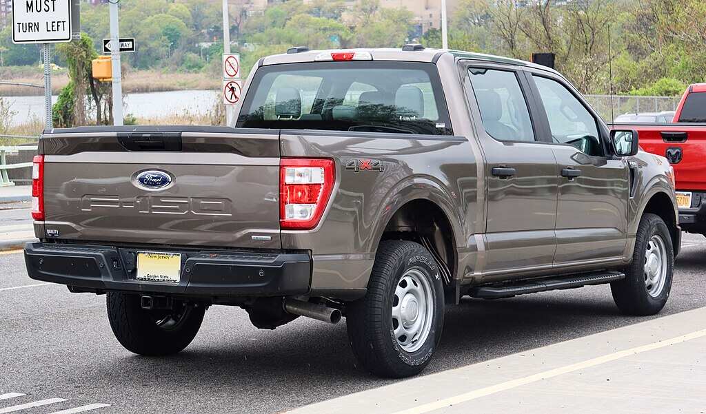 A gray 2021 Ford F-150 SuperCrew pickup truck parked on a street, showing the rear three-quarter view with visible tailgate, taillights, and bed.