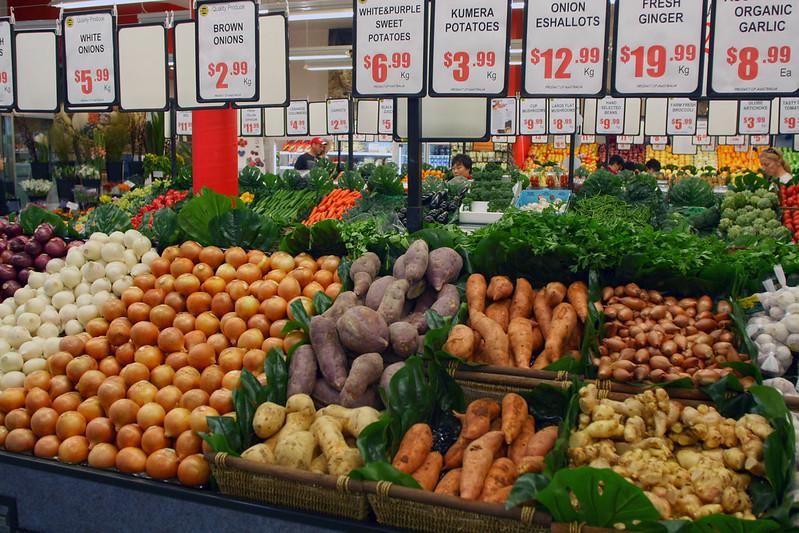 Fresh produce display at Sydney Fish Market featuring onions, potatoes, ginger, and garlic with price signs in Australian dollars.