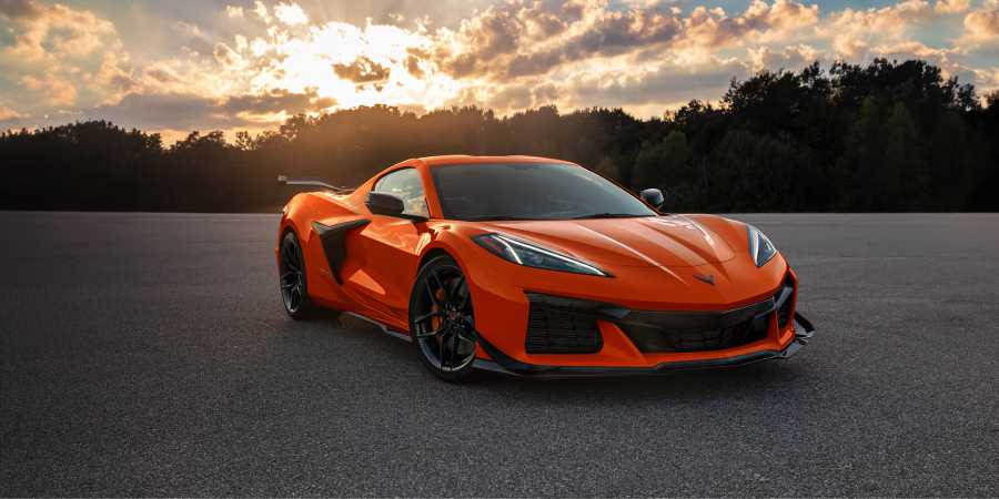 Orange 2025 Chevrolet Corvette Z06 supercar parked on asphalt at sunset with dramatic sky in background