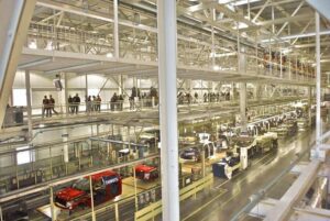 Interior view of the Ford Rouge Factory in Dearborn, Michigan, showing trucks on the assembly line and visitors observing from the upper-level tour walkway.