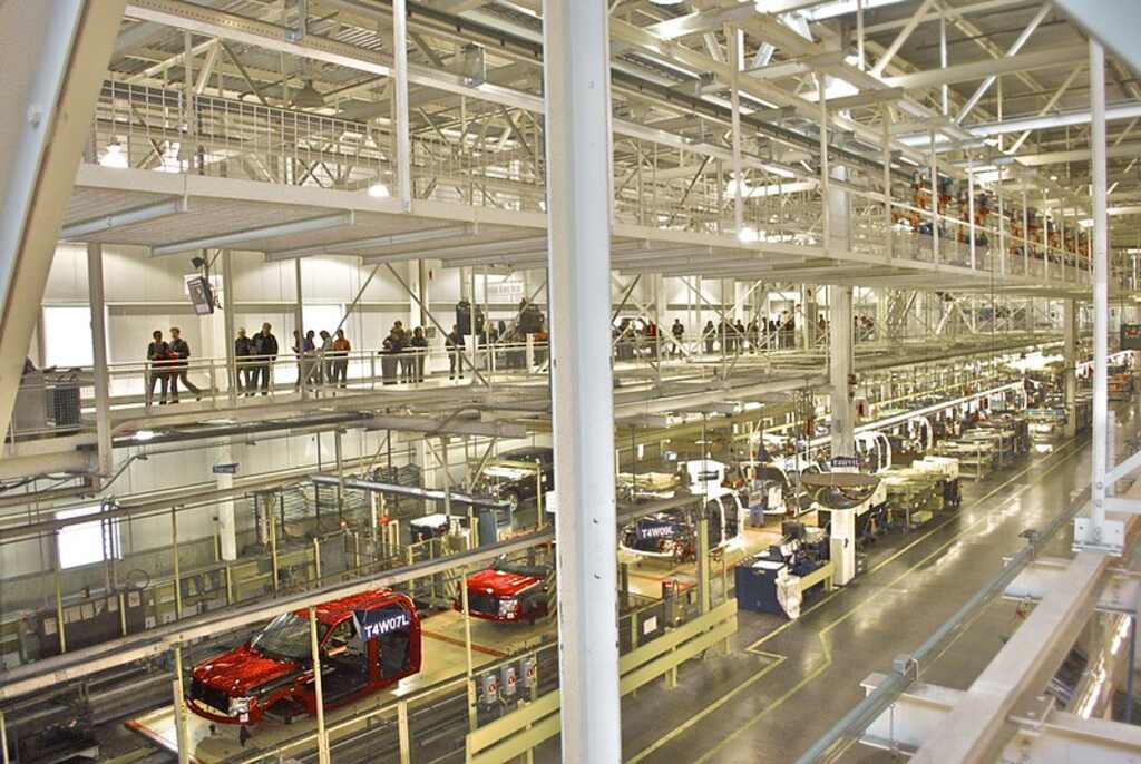Interior view of the Ford Rouge Factory in Dearborn, Michigan, showing trucks on the assembly line and visitors observing from the upper-level tour walkway.