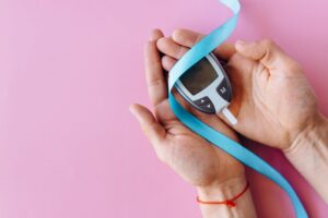 Hands holding a blood glucose meter with blue ribbon against pink background