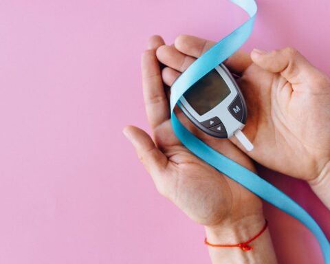 Hands holding a blood glucose meter with blue ribbon against pink background