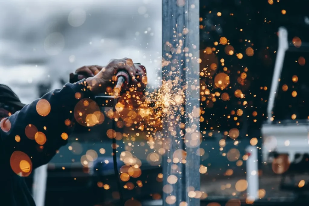 Close-up of a welder working with metal, creating bright orange sparks in a dark industrial environment, illustrating industrial processes that contribute to methane emissions.