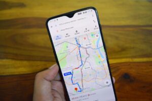 Smartphone showing Google Maps navigation route with traffic indicators and estimated travel time on a wooden table background.