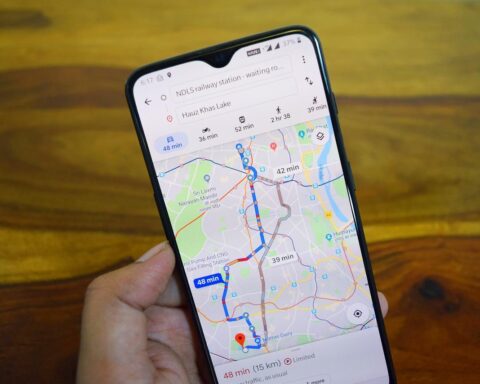 Smartphone showing Google Maps navigation route with traffic indicators and estimated travel time on a wooden table background.