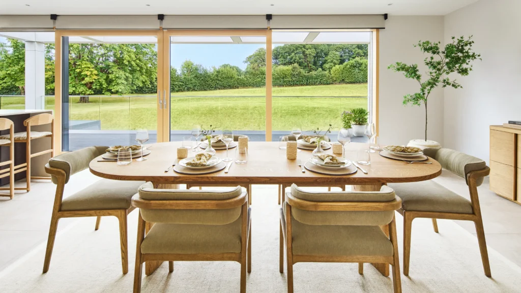 Upper-level dining room with bespoke wooden table, linen chairs, and abundant natural light from large windows and skylights.