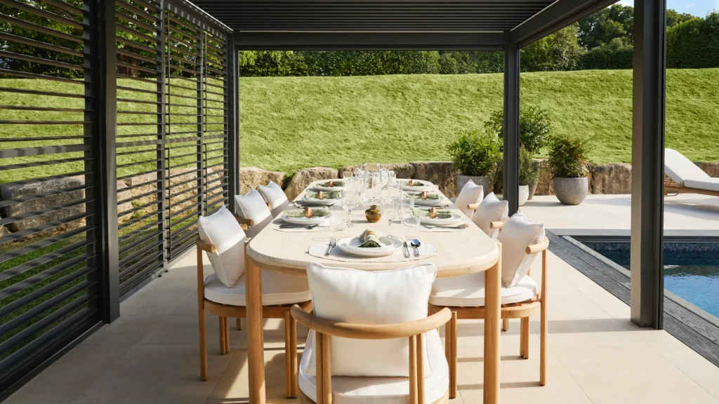 Outdoor circular teak dining table with modern chairs set in landscaped garden of the Omaze Surrey Hills house with countryside views.