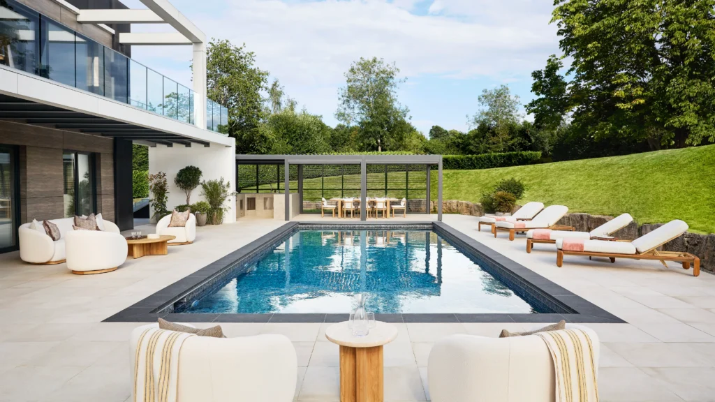 Heated outdoor swimming pool of the Omaze prize house with loungers, surrounded by landscaped gardens and contemporary architecture.