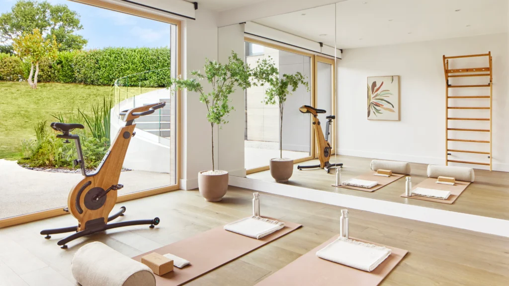 Home gym with wooden exercise equipment, yoga mat, and large windows overlooking garden, converted from one of the original bedrooms.