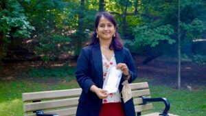 Rashmi Prakash, UBC biomedical engineering alumna, standing outdoors holding a compostable menstrual pad product while wearing a navy blazer over a floral dress.