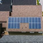 Aerial view of solar panels installed on the roof of a suburban house with neighboring homes visible
