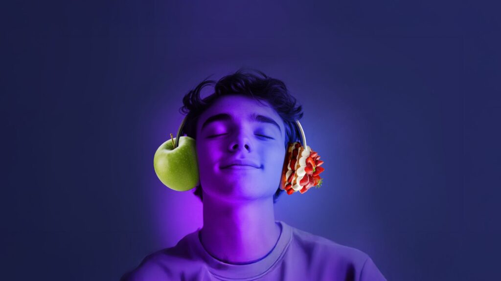 Person with closed eyes wearing headphones, with a green apple positioned at one ear and strawberries at the other ear, against a purple-blue background.