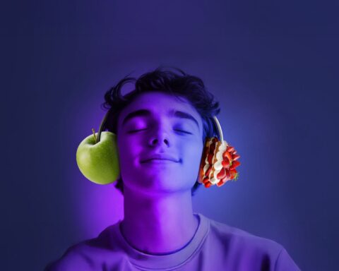 Person with closed eyes wearing headphones, with a green apple positioned at one ear and strawberries at the other ear, against a purple-blue background.