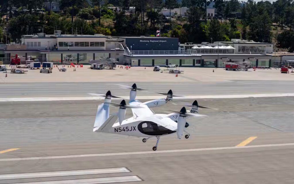 A white Joby Aviation electric vertical takeoff and landing (eVTOL) aircraft with six tilting propellers on the runway at Monterey Regional Airport.
