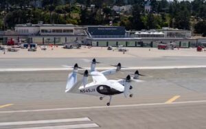A white Joby Aviation electric vertical takeoff and landing (eVTOL) aircraft with six tilting propellers on the runway at Monterey Regional Airport.