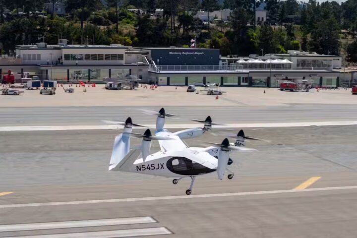 A white Joby Aviation electric vertical takeoff and landing (eVTOL) aircraft with six tilting propellers on the runway at Monterey Regional Airport.