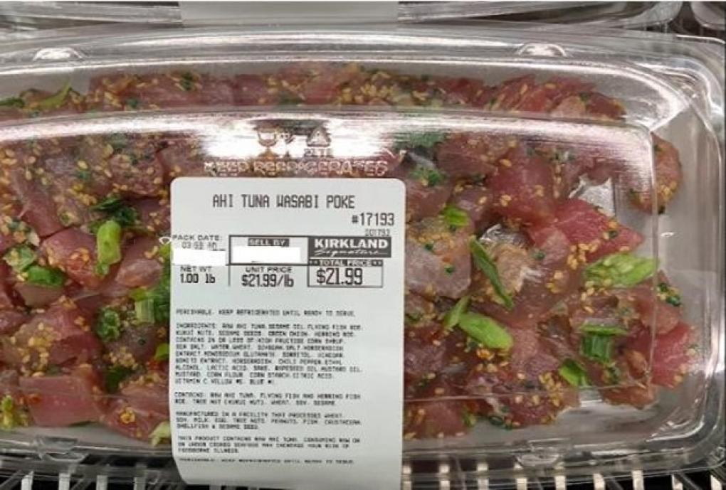 Clear plastic clamshell container of Kirkland Signature Ahi Tuna Wasabi Poke, labeled with pack and sell-by dates, recalled due to potential Listeria contamination from green onions.