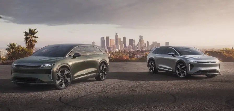 Two Lucid Gravity electric SUVs with aerodynamic designs parked on a hill overlooking Los Angeles skyline at sunset