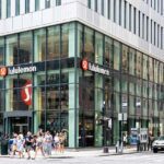 A busy Lululemon store on a New York City street corner with large glass windows and people walking by.
