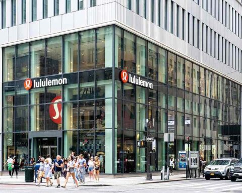 A busy Lululemon store on a New York City street corner with large glass windows and people walking by.