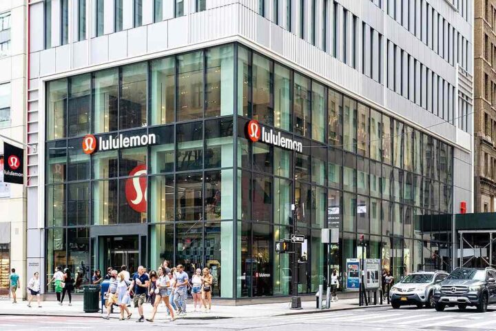 A busy Lululemon store on a New York City street corner with large glass windows and people walking by.