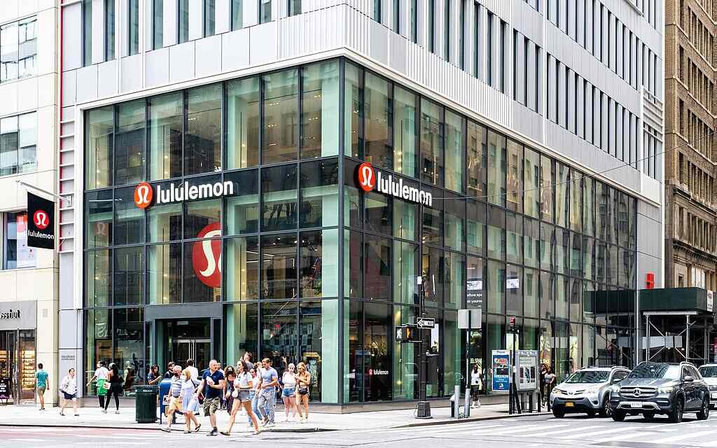 A busy Lululemon store on a New York City street corner with large glass windows and people walking by.