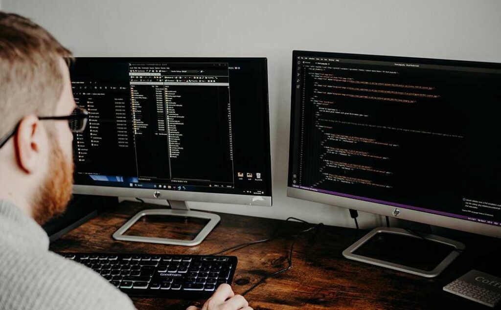 Person working at computer with multiple screens showing emails and spreadsheets, illustrating the multitasking environment that makes detecting phishing emails more difficult.