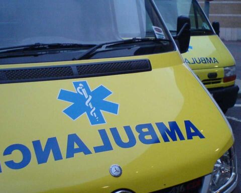 Close-up view of yellow London ambulance vehicle with blue NHS star of life medical symbol visible on the side.