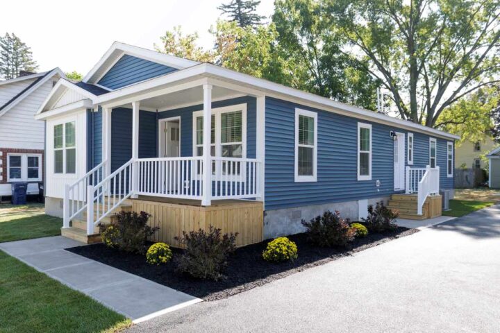 Factory-built CrossMod home with pitched roof, front porch, and attached garage installed on vacant lot in New York pilot community