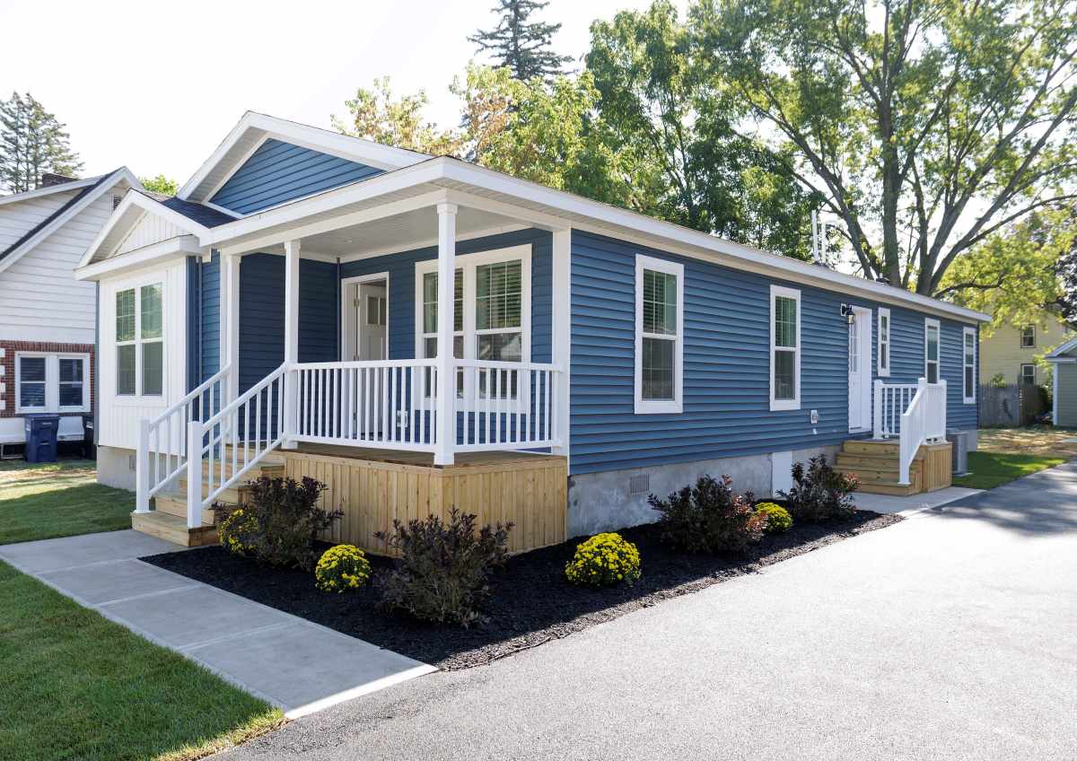 Factory-built CrossMod home with pitched roof, front porch, and attached garage installed on vacant lot in New York pilot community