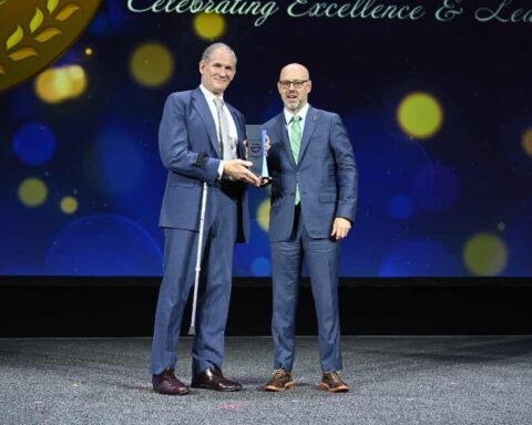 MTA Chair and CEO Janno Lieber accepting the American Public Transportation Association's 2025 Innovation Award from APTA Awards Committee Chair Richard W. Andreski on stage at the awards ceremony.