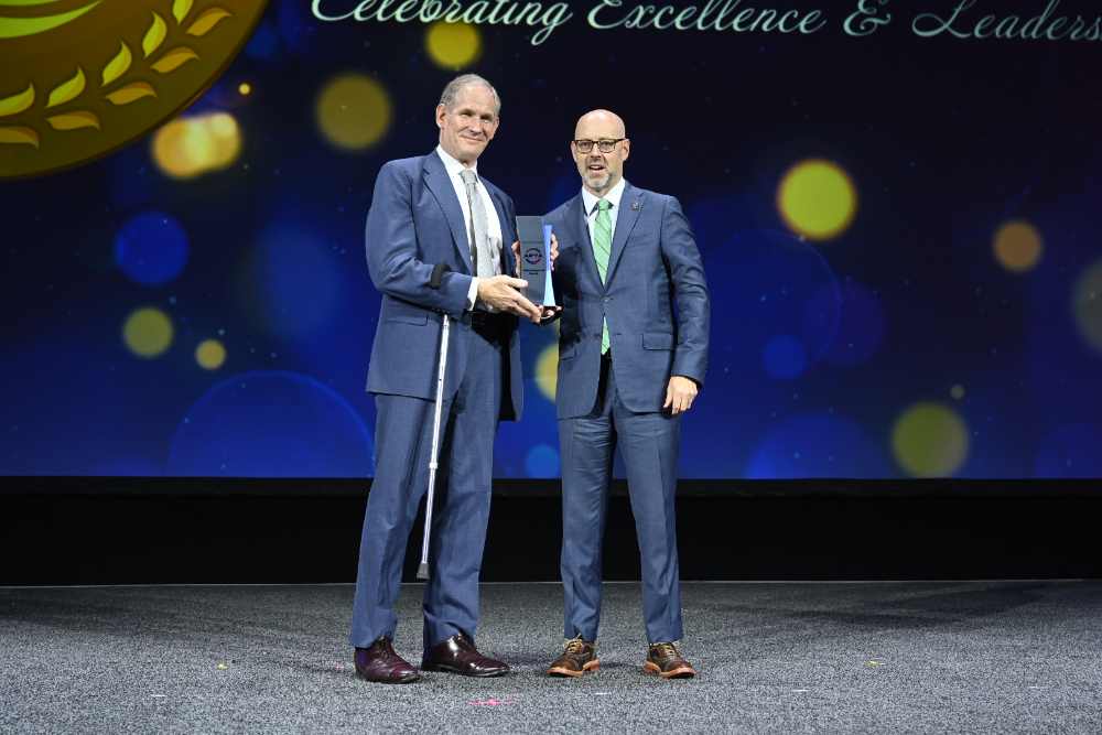 MTA Chair and CEO Janno Lieber accepting the American Public Transportation Association's 2025 Innovation Award from APTA Awards Committee Chair Richard W. Andreski on stage at the awards ceremony.