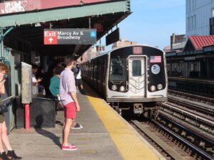 NYC subway train arriving at Marcy Avenue station in Williamsburg with passengers waiting on the platform
