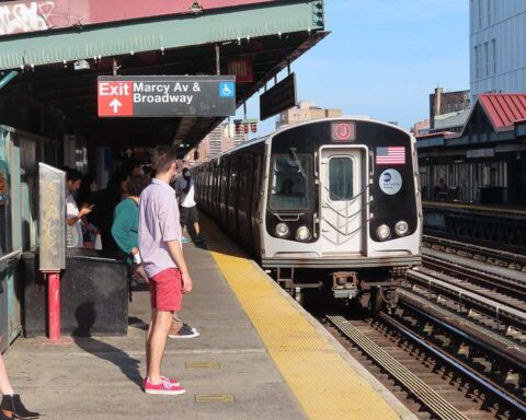 NYC subway train arriving at Marcy Avenue station in Williamsburg with passengers waiting on the platform