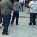 Several people with varying body types standing in what appears to be a shopping mall or public space, photographed from behind.