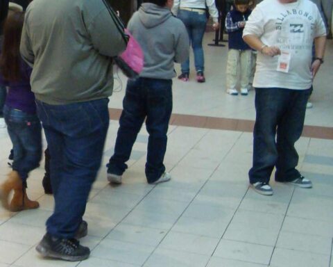 Several people with varying body types standing in what appears to be a shopping mall or public space, photographed from behind.
