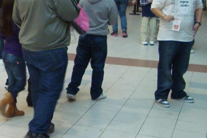 Several people with varying body types standing in what appears to be a shopping mall or public space, photographed from behind.