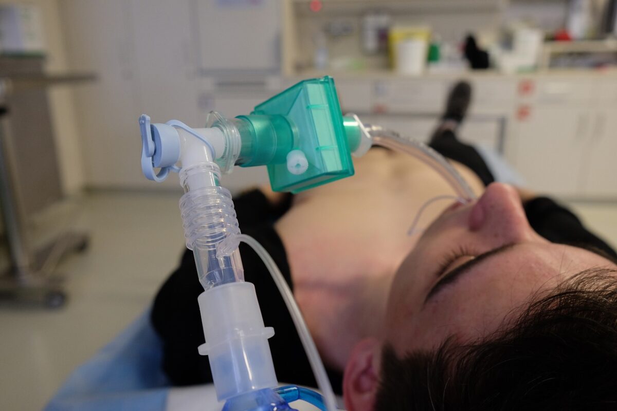 Medical oxygen mask with green mouthpiece attached to a breathing apparatus being used on a patient lying down in a clinical setting