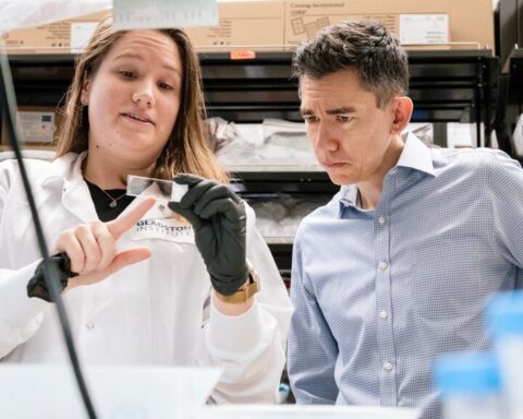 Two researchers in a laboratory setting - a female scientist in a white lab coat on the left and a male scientist in a blue checkered shirt on the right, examining laboratory equipment in what appears to be a neuroscience research facility